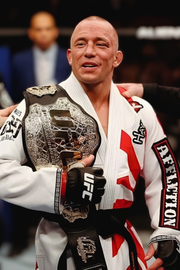 Person in a white martial arts uniform holding a championship belt with 'UFC' branding.
