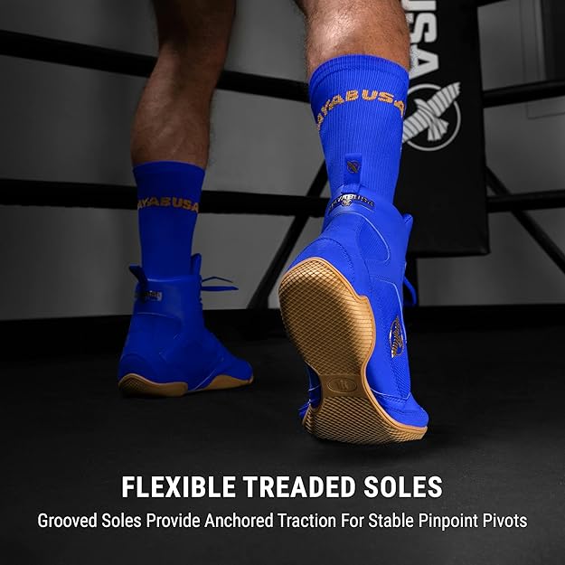 Blue boxing shoes with gold soles worn by a person, on a dark background with visible branding.