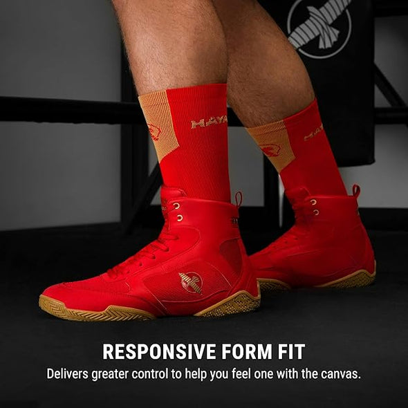 Red high-top boxing shoes with gold accents worn by a person, on a dark background.