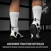 Person wearing white socks with black traction outsoles on a dark background