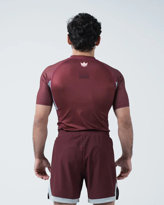 Person wearing a maroon sports outfit with a logo on the chest against a white background