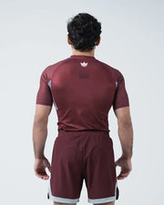 Person wearing a maroon sports outfit with a logo on the chest against a white background