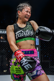 Boxer in Fairtex gear celebrating a victory in a dark arena setting