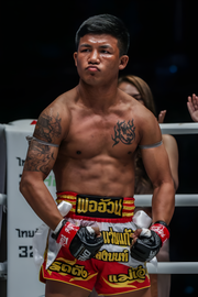 Athlete in red and yellow shorts with gloves, standing in a boxing ring.