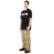 Person wearing a black t-shirt with text and beige cargo pants on a white background