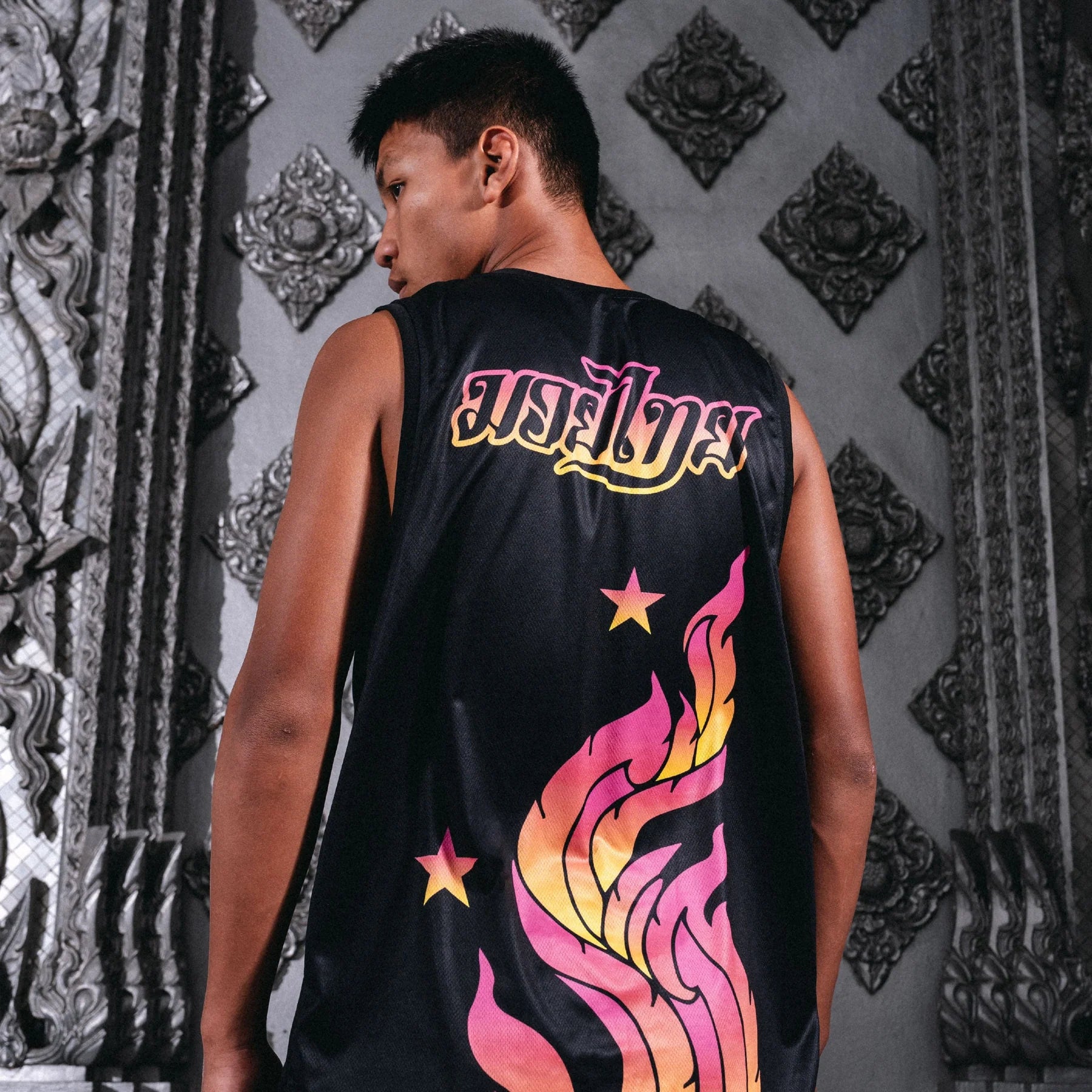 Person wearing a black sleeveless shirt with colorful designs and text against an ornate wall.