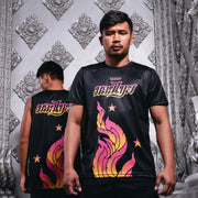 Man wearing a black t-shirt with colorful graphics and text, standing in front of a decorative silver wall.