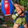 Person wearing green boxing gloves and shorts, punching a red and blue punching bag outdoors.