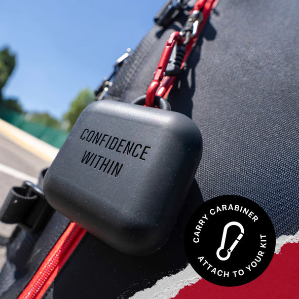 Black carabiner with 'CONFIDENCE WITHIN' text attached to a bag outdoors.