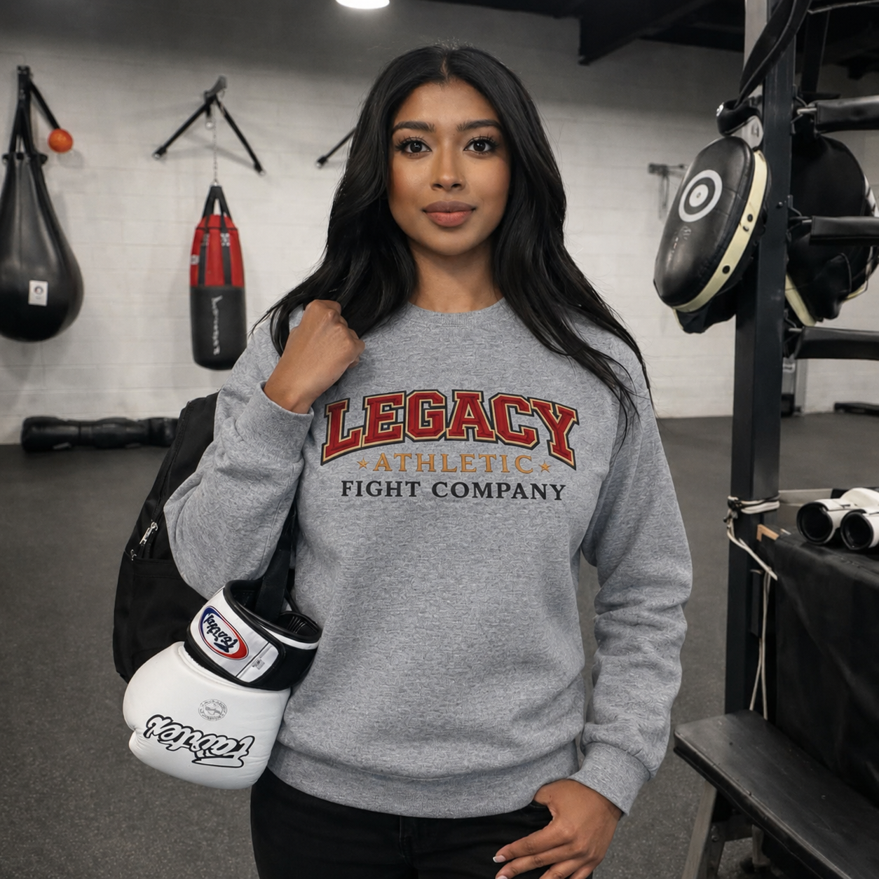Woman wearing a gray 'Legacy Athletics Fight Company' sweatshirt in a gym setting.