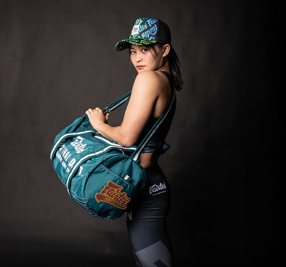 Person holding a teal duffel bag with branding against a dark background