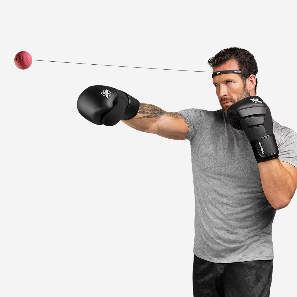 Man wearing boxing gloves and a headband, using a boxing ball on a white background