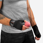 Person wearing black boxing hand wraps holding a pink exercise ball, with a gray shirt and black pants.