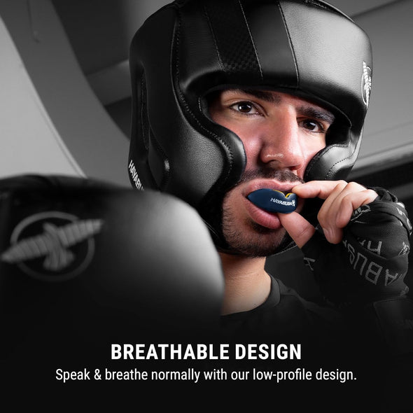 Person wearing a black boxing helmet with a visible brand logo, holding a microphone close to their mouth.