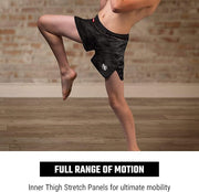 Person wearing black athletic shorts with a brand logo, standing on one leg against a brick wall.