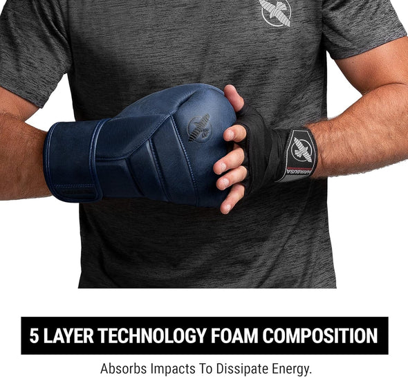Person wearing a black glove with a brand logo, holding a blue glove, on a gray background.