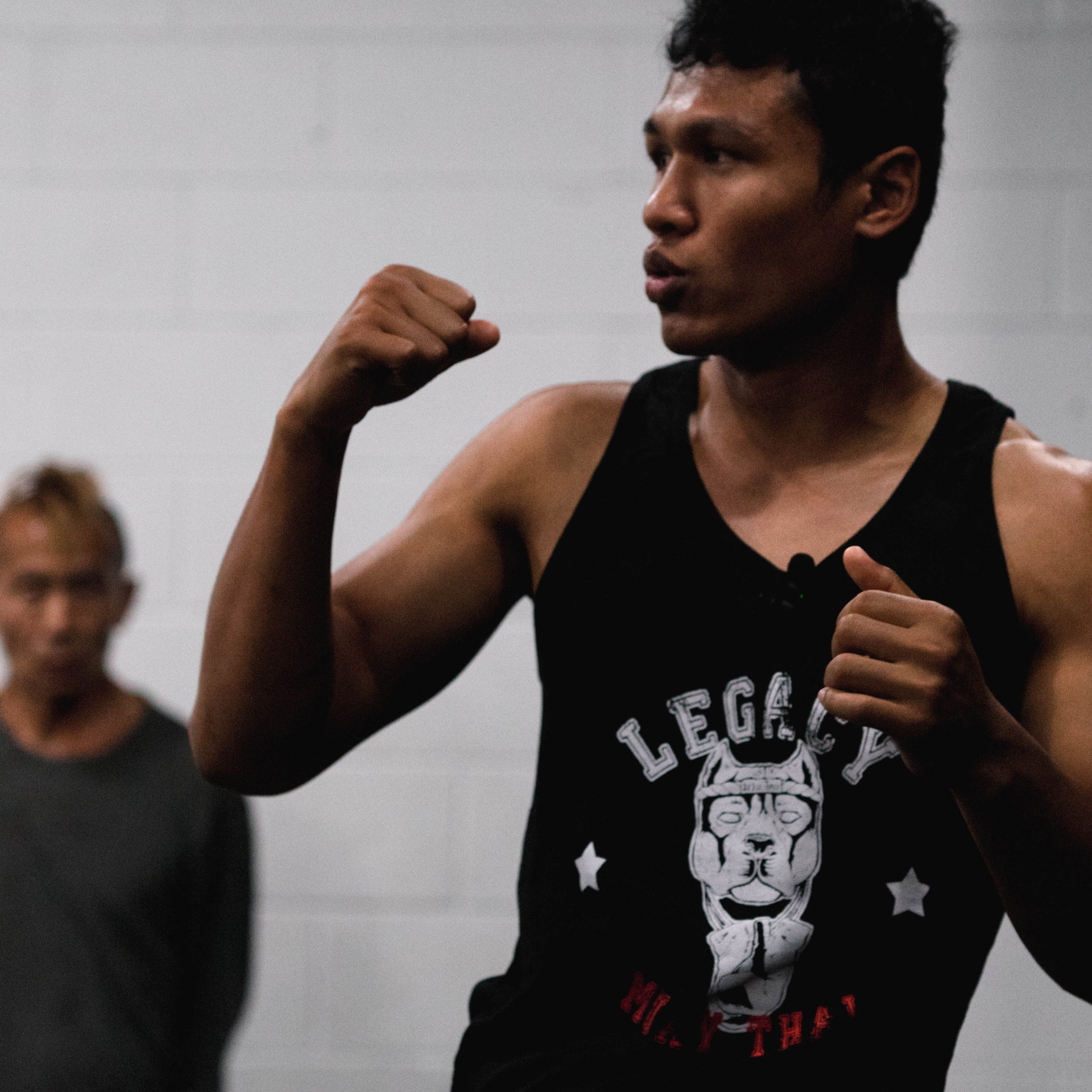 Person in a black tank top with a graphic design, flexing their arm in a gym setting.