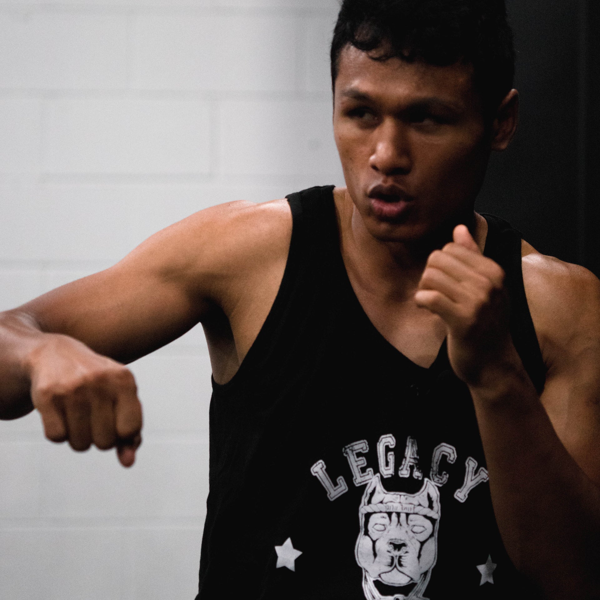 Man in a black tank top with 'Legacy' logo in a gym setting
