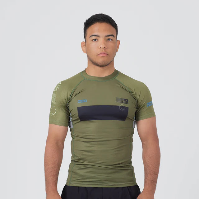 Man wearing an olive green athletic shirt with a black stripe and black shorts on a white background