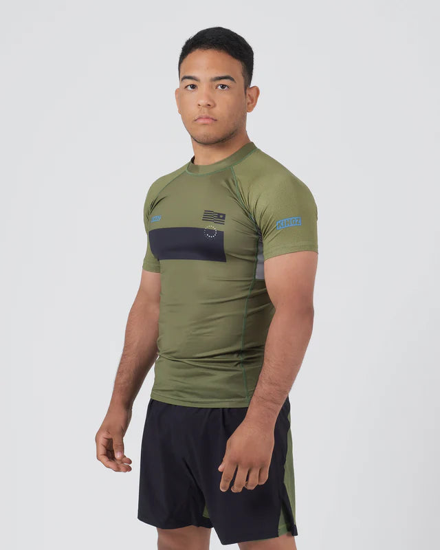 Man wearing an olive green athletic shirt with a logo on a white background