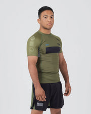 Man wearing an olive green athletic shirt and black shorts with a logo on a white background