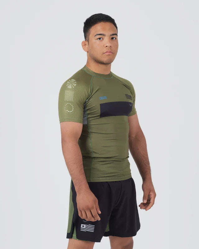 Man wearing an olive green athletic shirt and black shorts with a logo on a white background