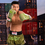 Boxer in green Yokkao boxing gloves and shorts posing in front of shipping containers.
