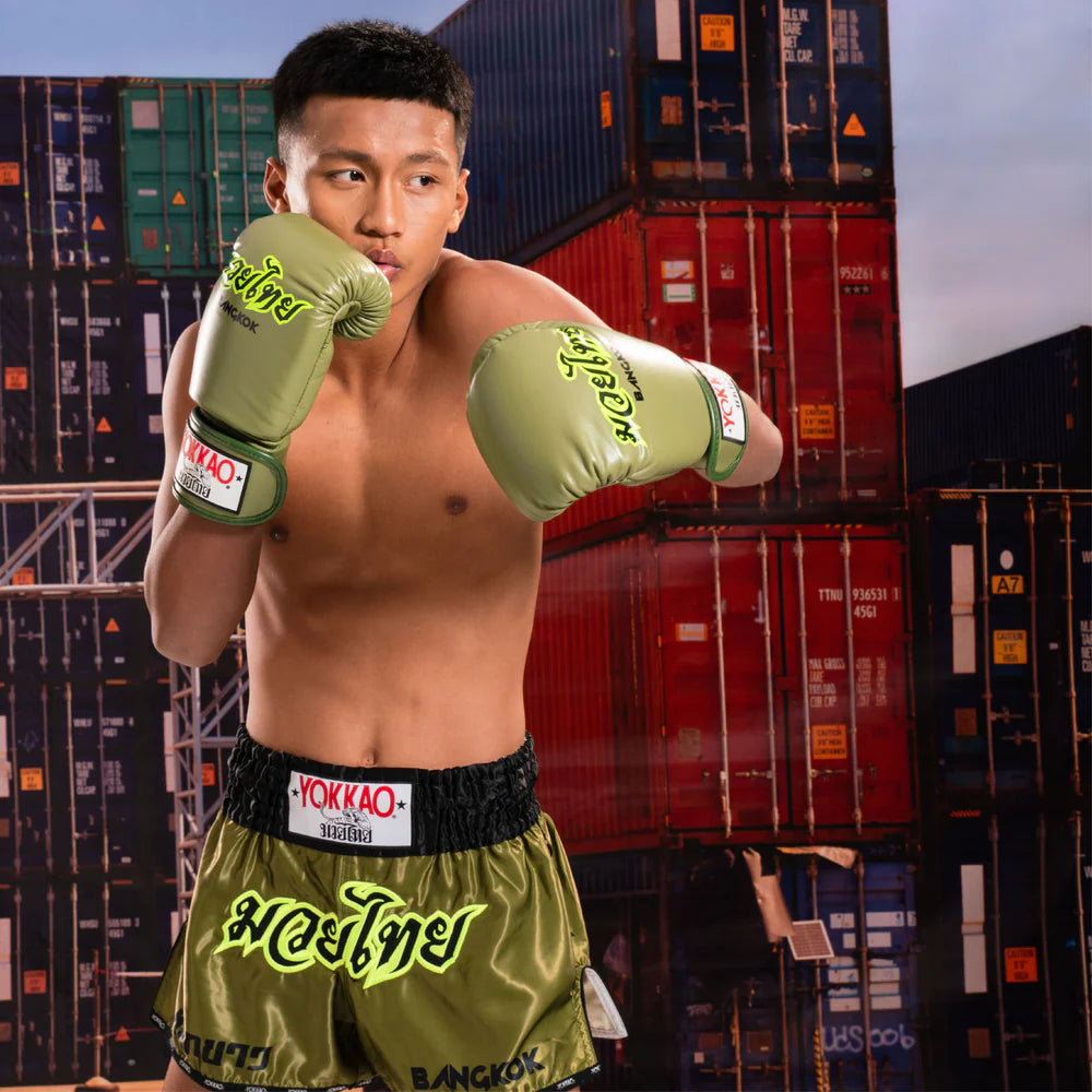 Boxer in green Yokkao boxing gloves and shorts posing in front of shipping containers.
