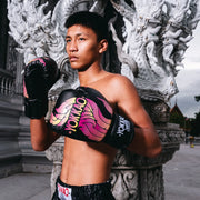 Person wearing boxing gloves and shorts with a colorful design, standing in front of ornate stone architecture.