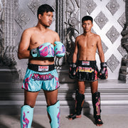 Two individuals in colorful Yokkao boxing gear standing against a decorative wall.