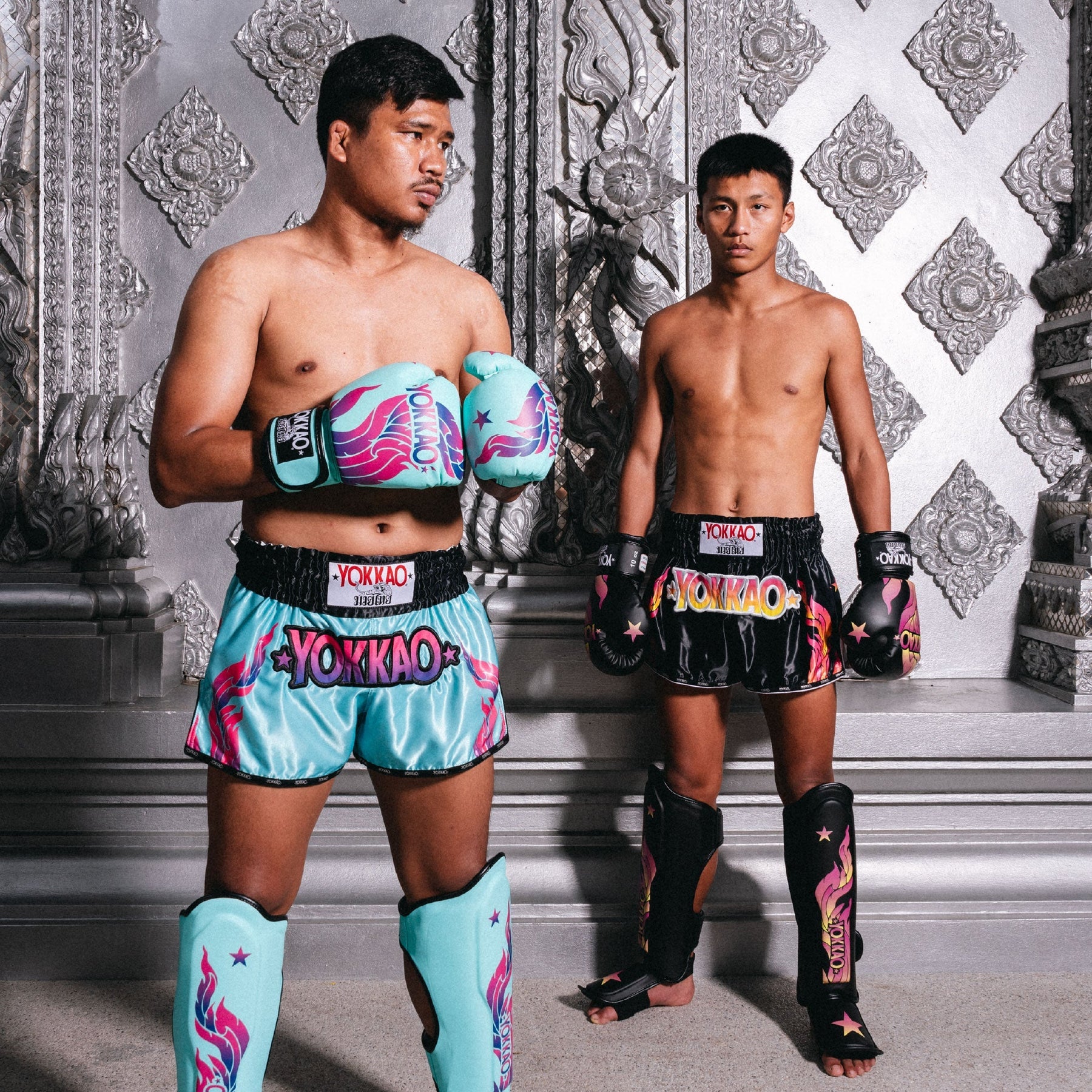Two individuals in colorful Yokkao boxing gear standing against a decorative wall.