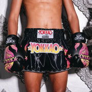 Person wearing black Yokkao boxing shorts and gloves on a decorative background