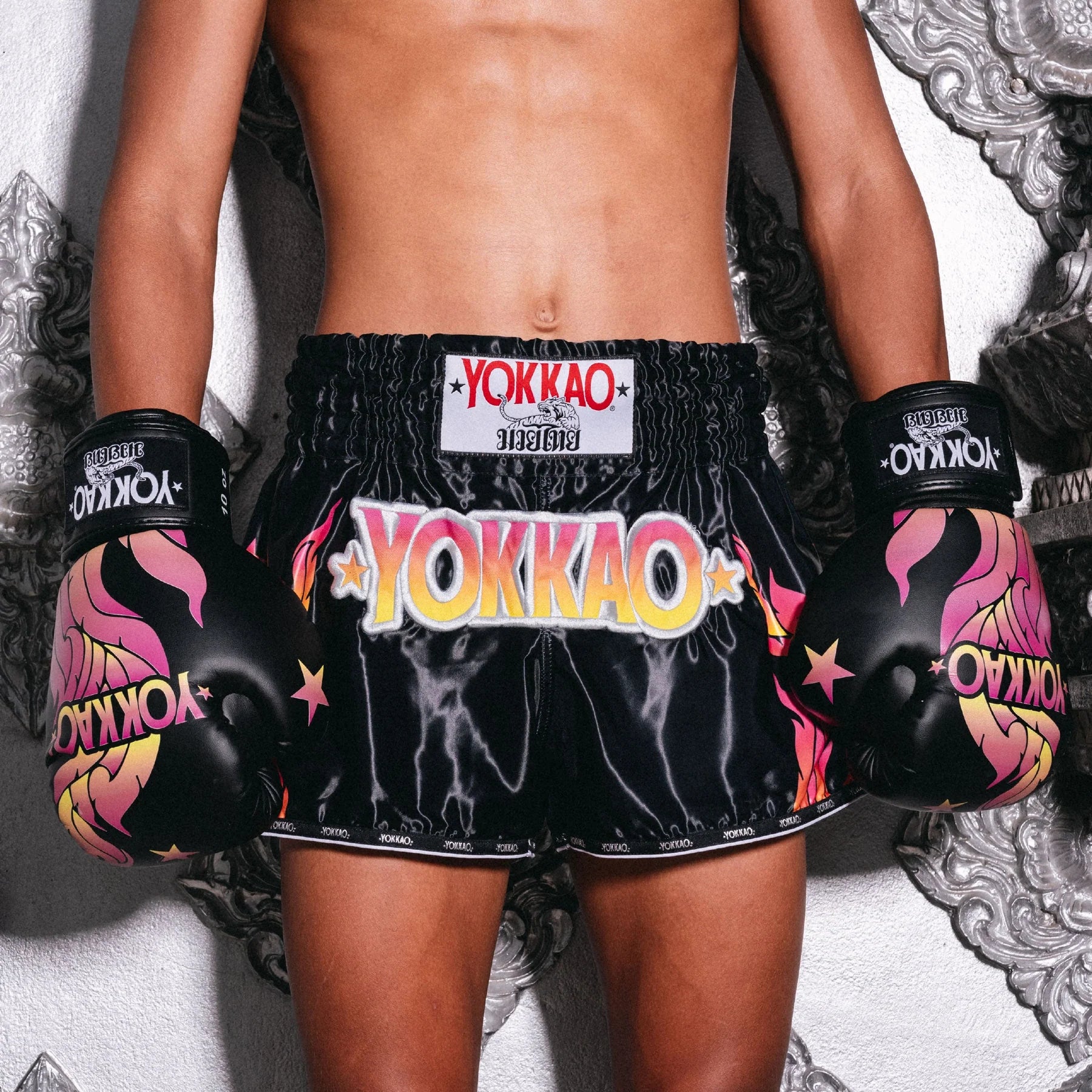 Person wearing black Yokkao boxing shorts and gloves on a decorative background