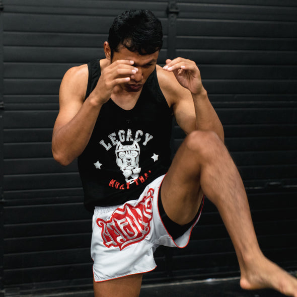 Person wearing a black tank top with 'Legacy' and white shorts with red text, posing against a dark background.