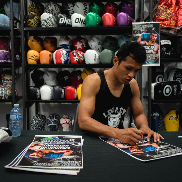 Person signing autographs at a table with boxing memorabilia in the background