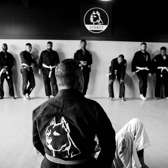Official Team Legacy BJJ Gi in black, featuring a 450 GSM Pearl Weave Plus jacket, 10 oz cotton drill pants, reinforced stitching, and includes a white belt and drawstring bag.