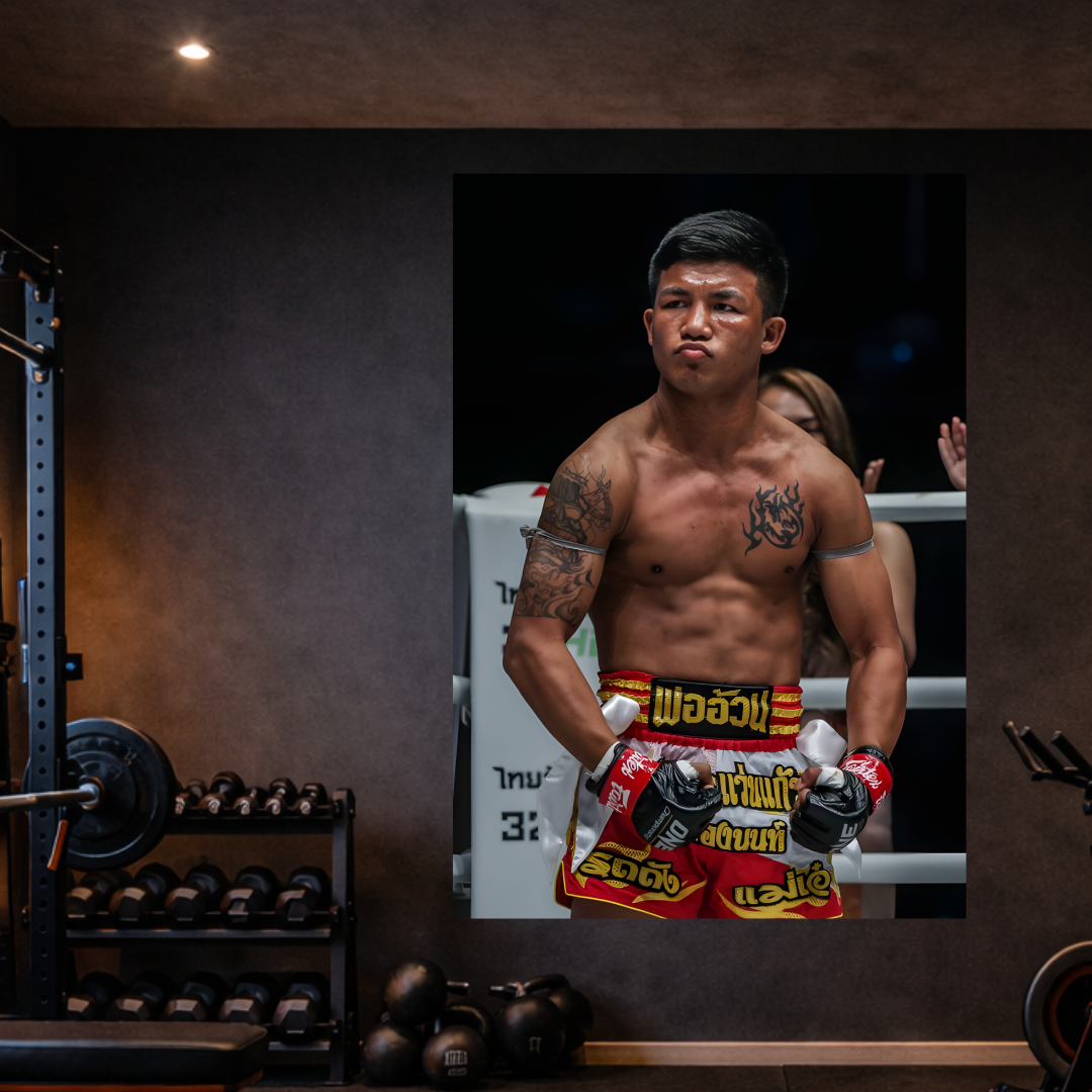 Boxer in red and yellow shorts standing in a boxing ring with gym equipment in the background.