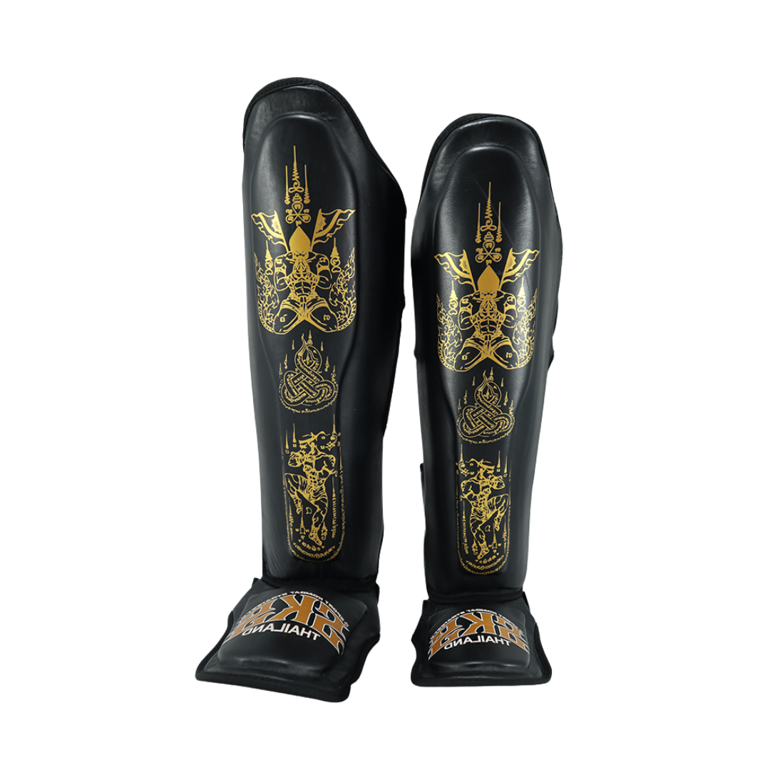 Black shin guards with gold designs on a white background