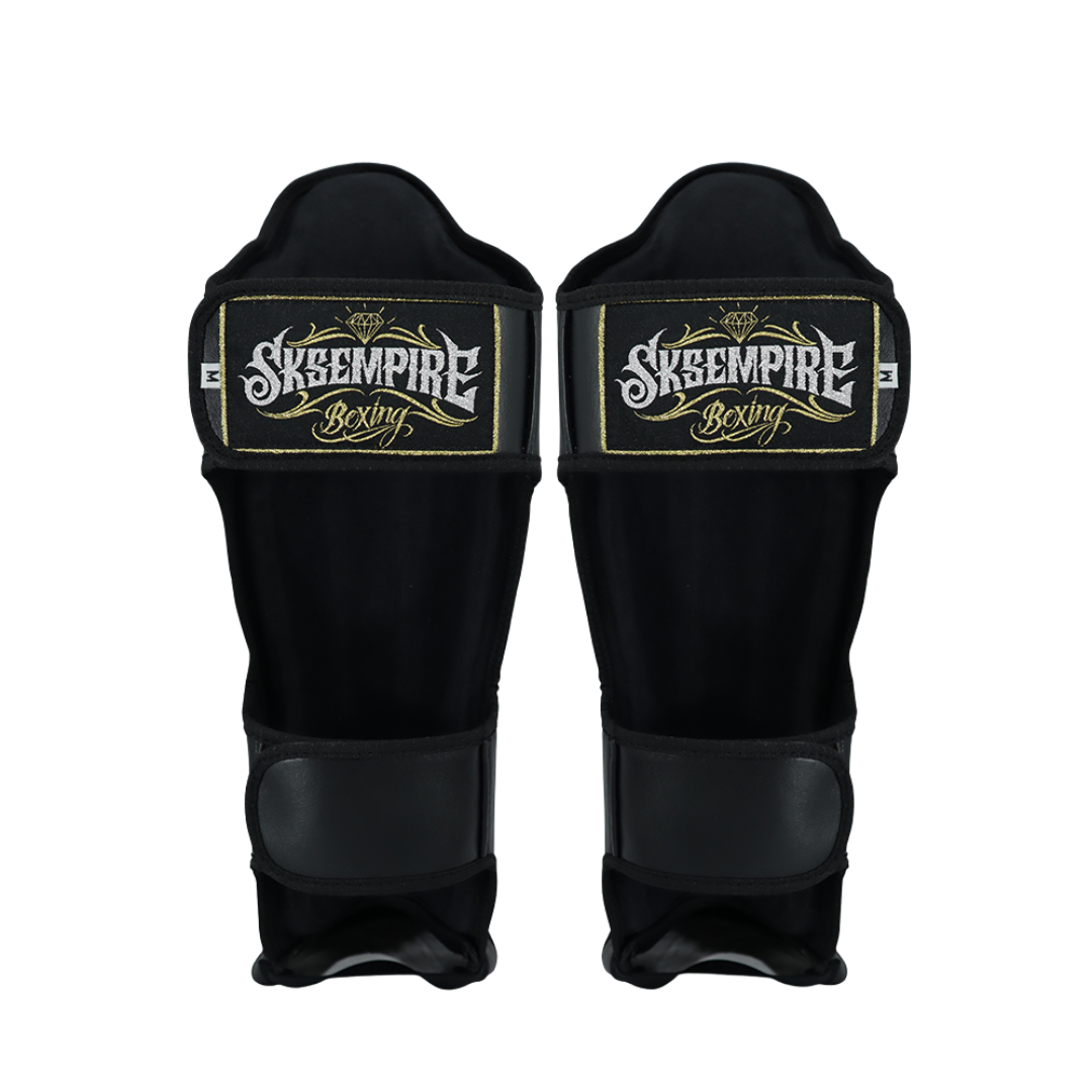 Pair of black shin guards with 'Sksempire Boxing' logo on a white background