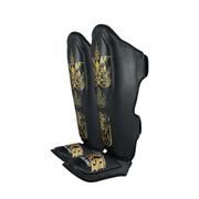 Black shin guards with gold designs on a white background