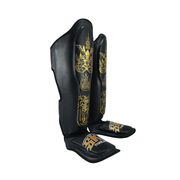 Black shin guards with gold designs on a white background