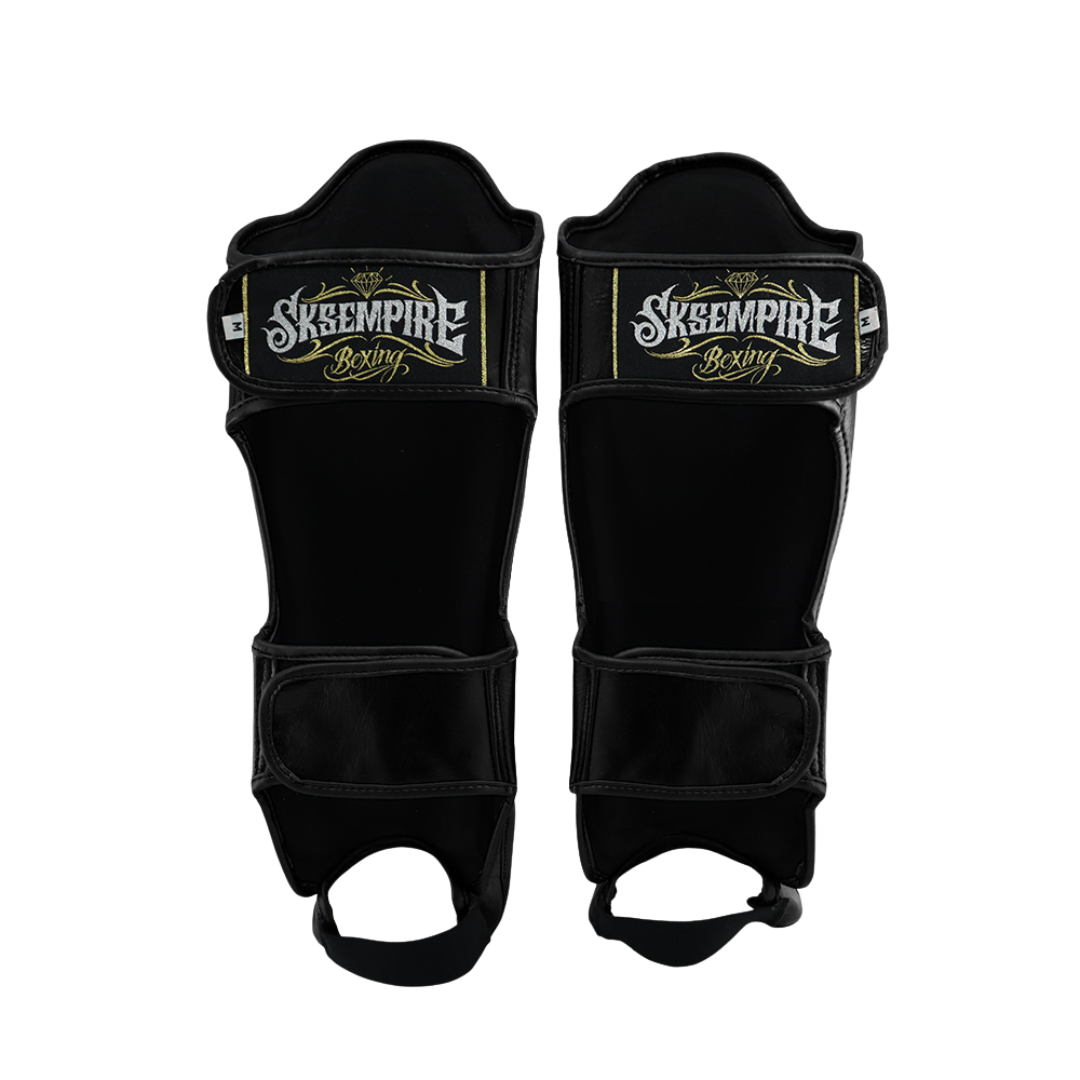 Pair of black shin guards with 'Skeempire Boxing' branding on a white background