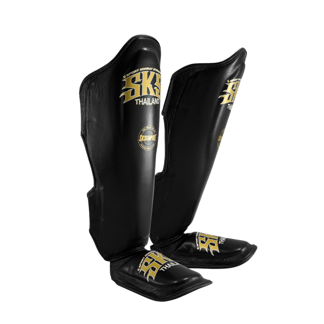 Black shin guards with gold branding on a white background