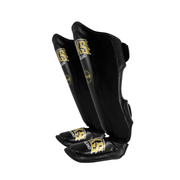 Pair of black shin guards with gold logos on a white background